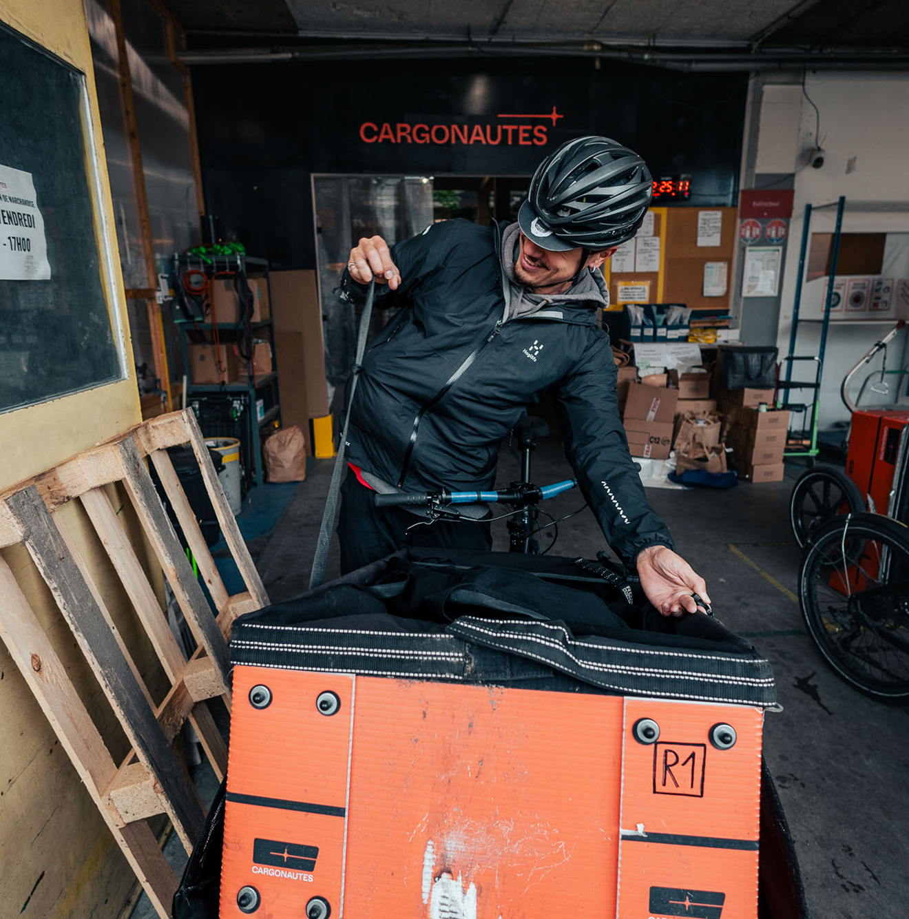Un livreur bouclant la caisse de son Cargo un grand sourir aux lèvres.